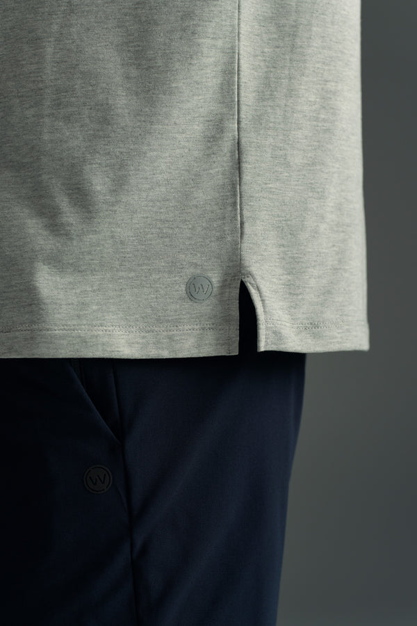 Close-up of a person wearing the light gray WearEver Outbound Polo and dark pants. The polo features a small side slit and subtle circular logo near the hem, while the pants show a similar small WearEver logo.
