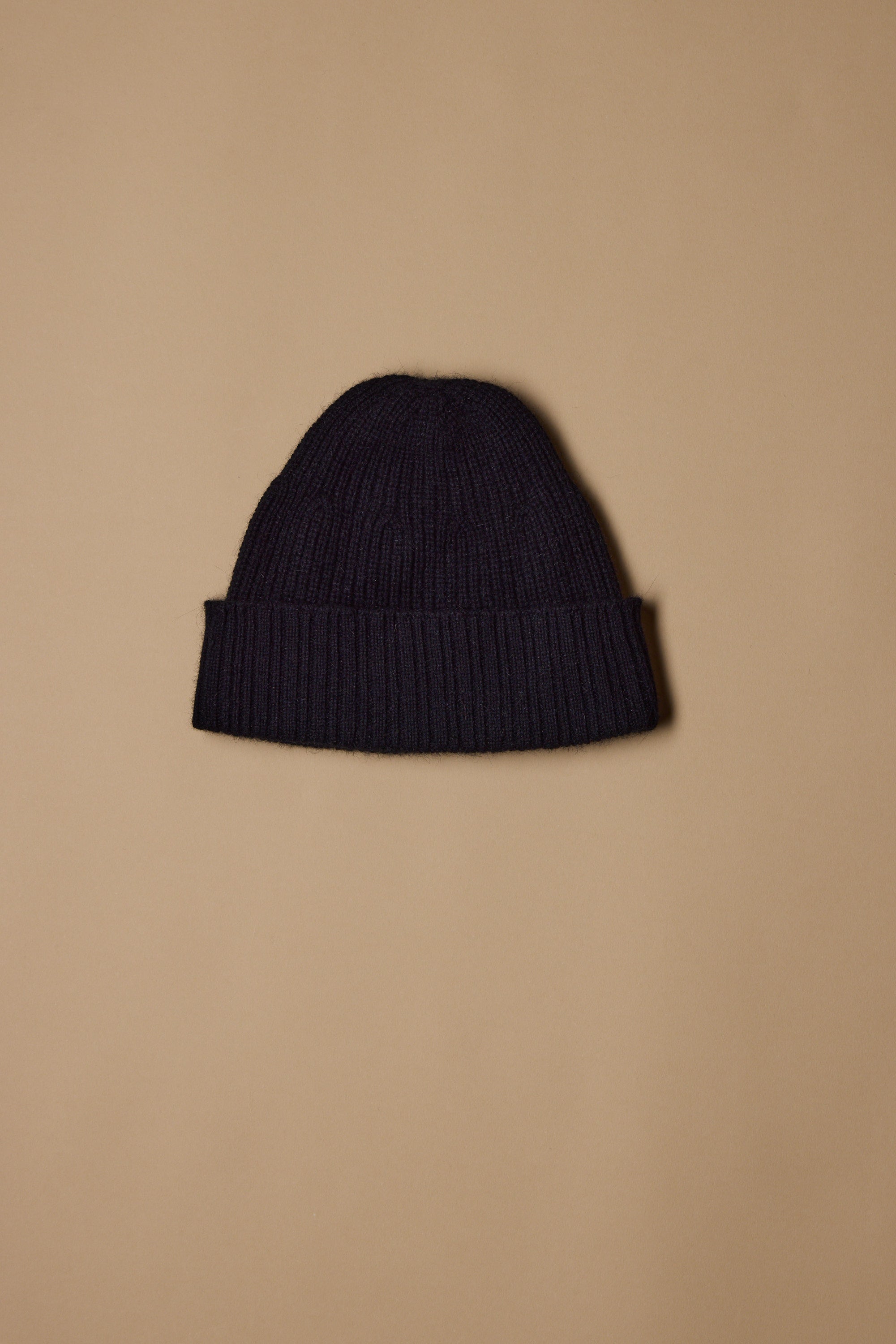 The NZ Made Perino Beanie by Woolyarns Perino, crafted from luxurious merino possum silk with a folded brim, is displayed centered on a plain beige background.