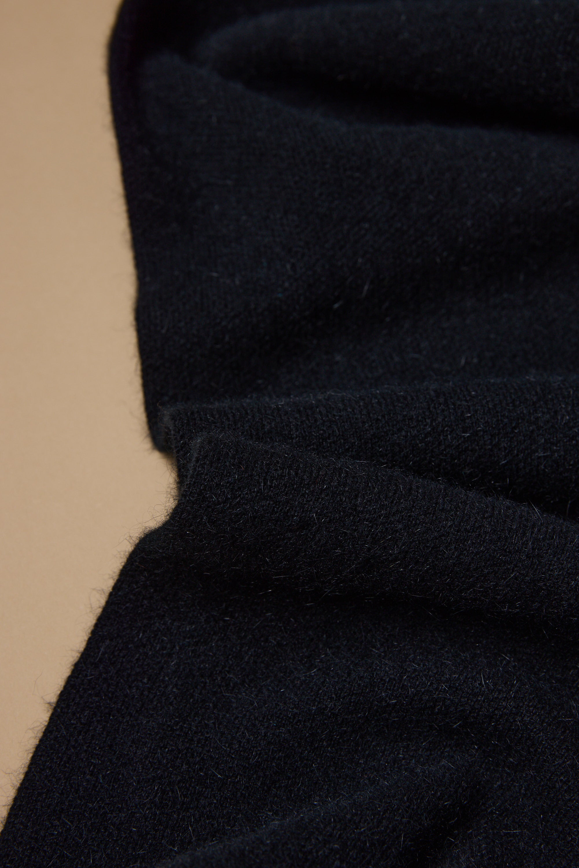 A close-up of the NZ Made Perino Scarf by Woolyarns Perino, showing the soft texture and fibers of its black merino possum silk blend fabric on a beige surface.