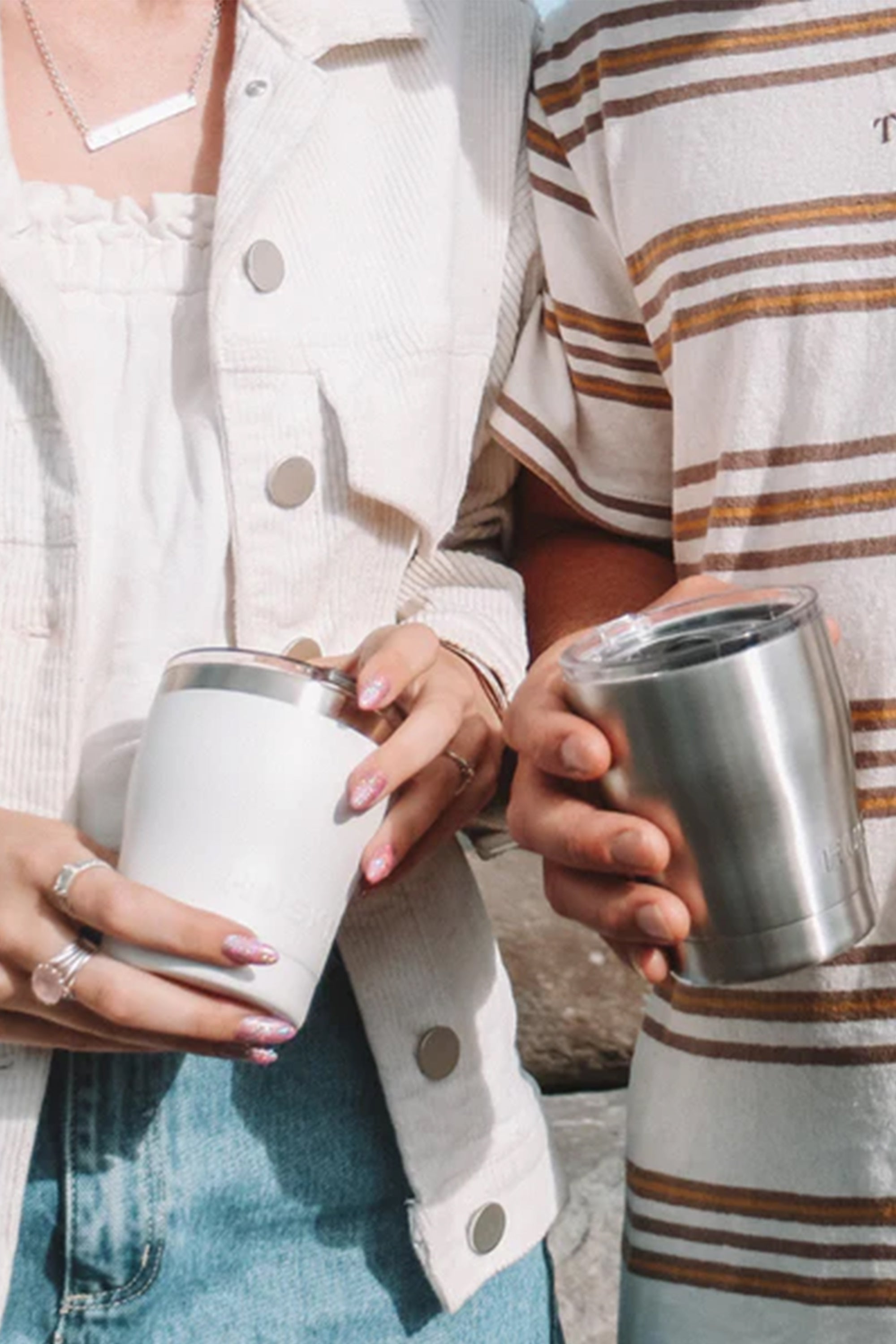 Two people stand side by side, each holding a Huski Short Tumbler 2.0 by Huski. One wears a white jacket with painted nails; the other has on a striped shirt. Their faces are not visible.