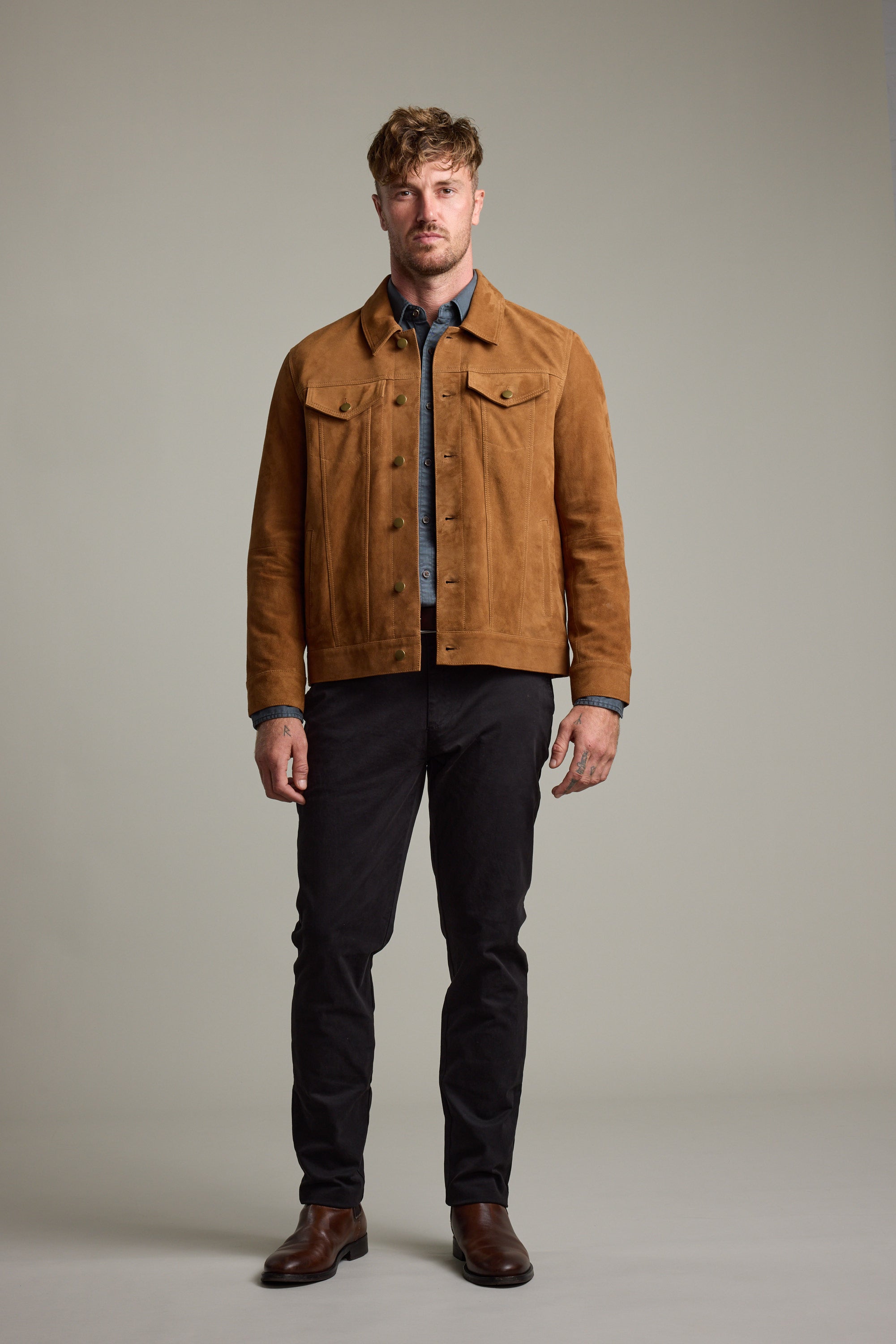 Man wears Barkers Jackson Suede Trucker jacket, blue shirt, black pants, and brown boots.