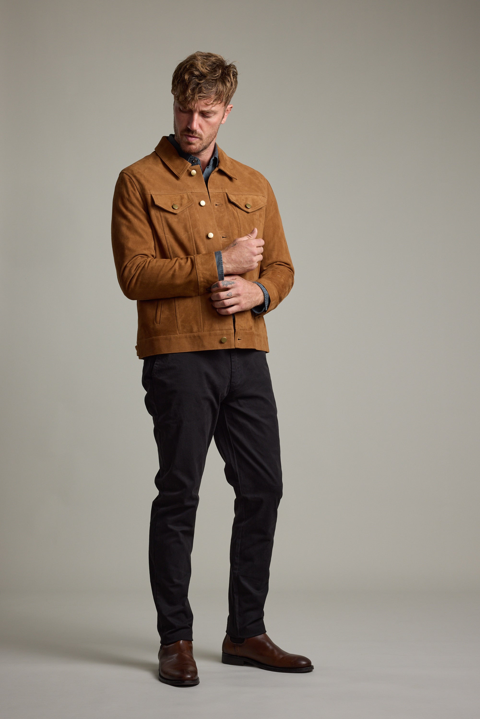 Man in Barkers Jackson Suede Trucker, black pants, and brown shoes on a plain background.