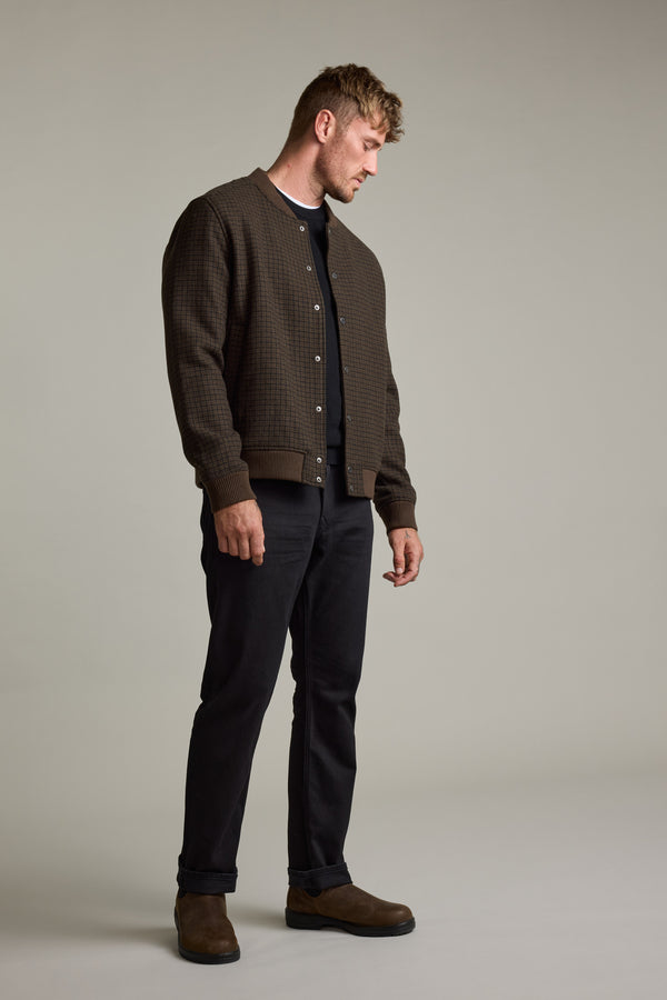 Man in Barkers Leland Wool Bomber Jacket with black shirt, pants, and brown boots looking down.