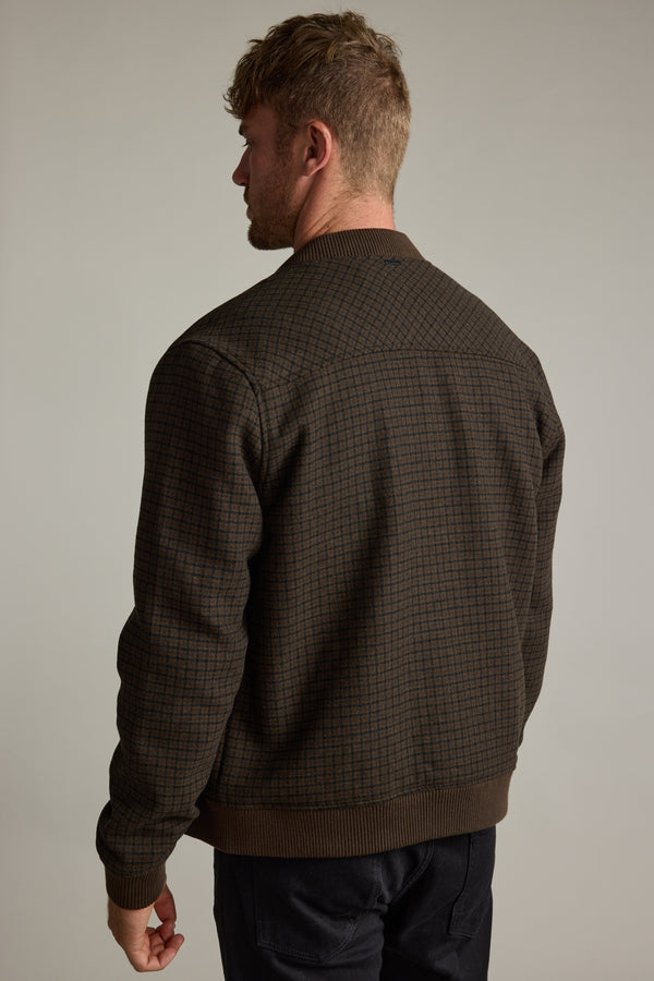 Man facing away in a Barkers Leland Wool Bomber Jacket and dark pants, plain background.