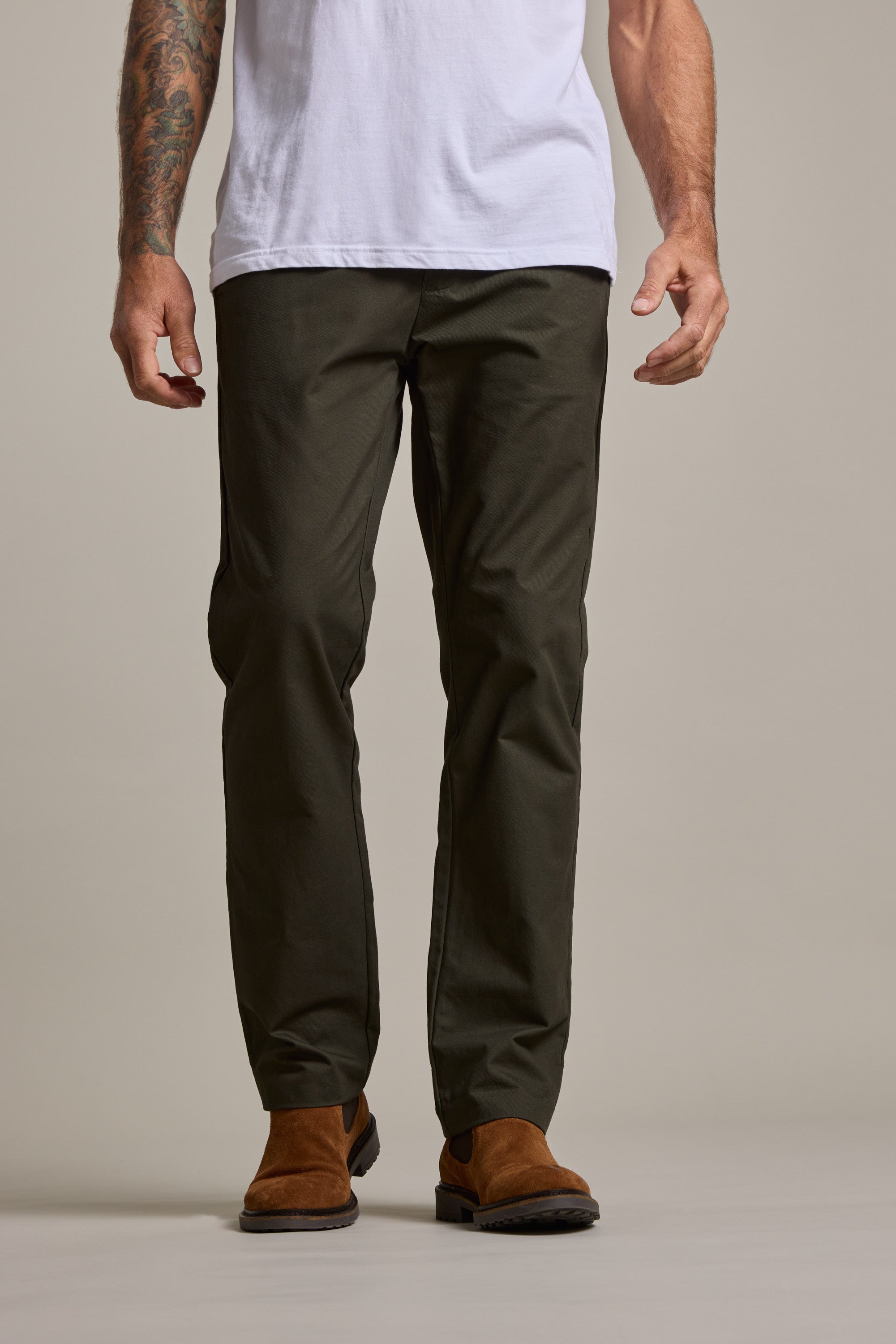 A person in Barkers Dundas Chino trousers (relaxed fit, dark green cotton twill), a white T-shirt, and brown suede shoes stands against a plain background, their forearms—one with a tattoo—visible.