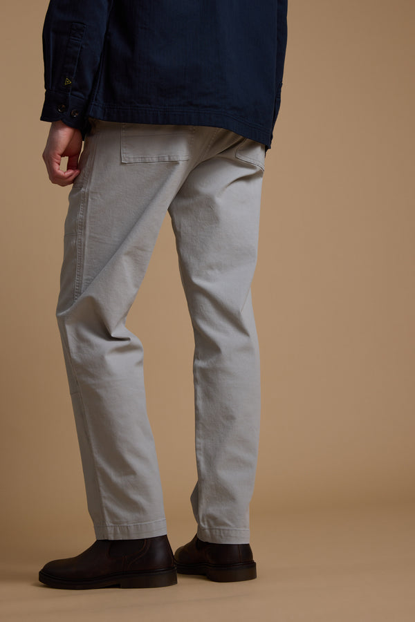 A person stands with their back to the camera, showing only the lower half of their body, wearing Barkers Tidal GD Utility Pant in light grey against a plain beige backdrop.