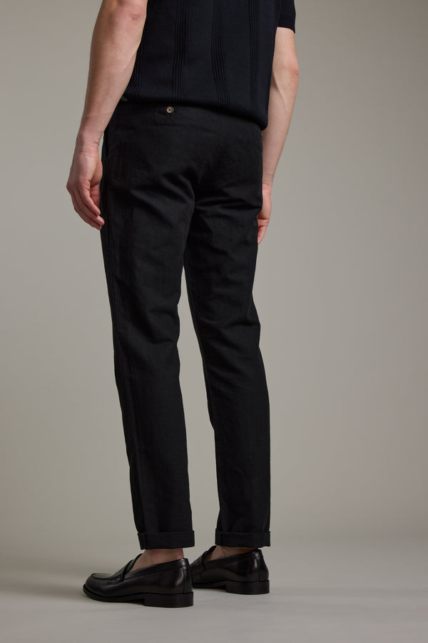 A person wearing Barkers’ Newman Linen Pant in black, paired with a short-sleeved black top and black dress shoes, stands facing away from the camera against a plain background.