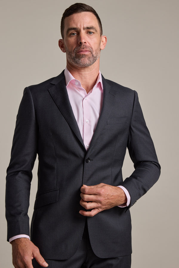 A man with short dark hair and a beard wears a Barkers Mayfair ZQ Suit Jacket and a light pink dress shirt, standing against a plain light background while buttoning his jacket.