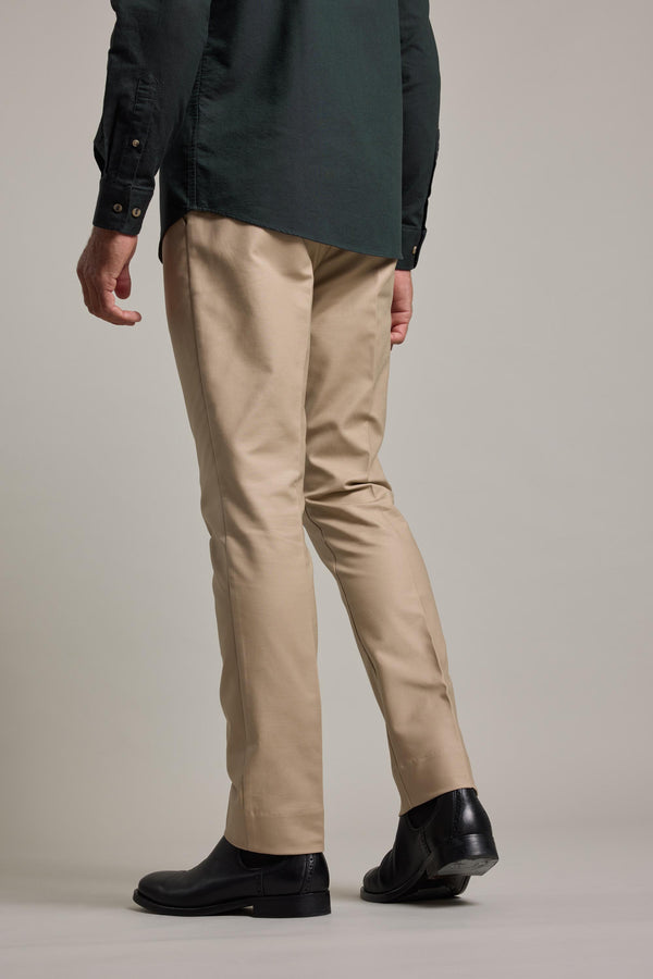 A person stands facing away from the camera against a plain light background, wearing Barkers Lyndon Cotton Pants in tan, a dark green button-up shirt, and black shoes.
