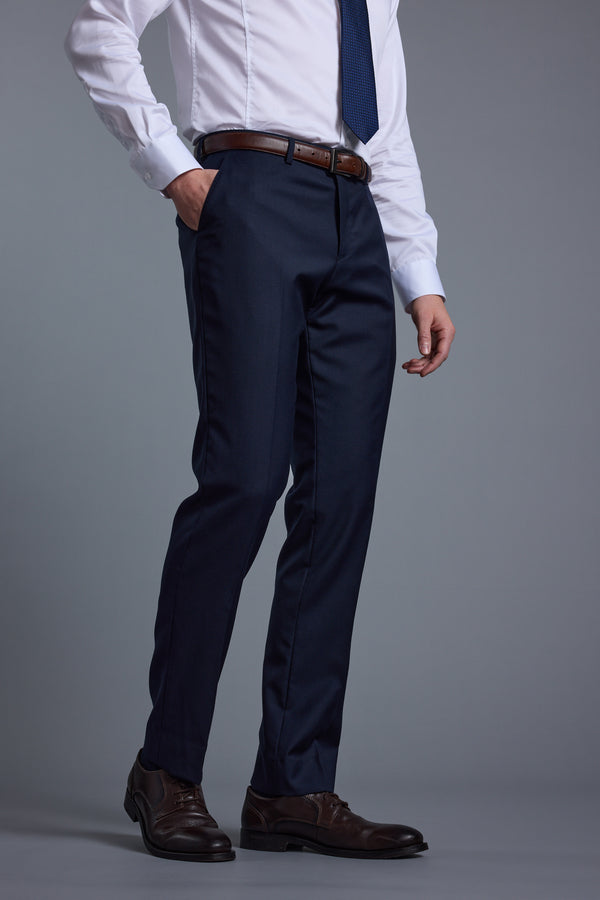 A person wearing Barkers’ Mayfair ZQ Suit Trouser stands against a plain gray background, paired with a white dress shirt, navy tie, brown leather belt, and shoes. The individual’s head is not visible in the photo.