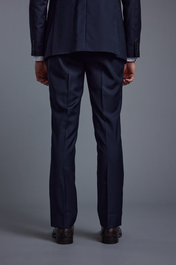 A person wearing Barkers’ Mayfair ZQ Suit Trousers with a dark navy three-piece suit and black shoes stands with their back to the camera against a plain gray background.