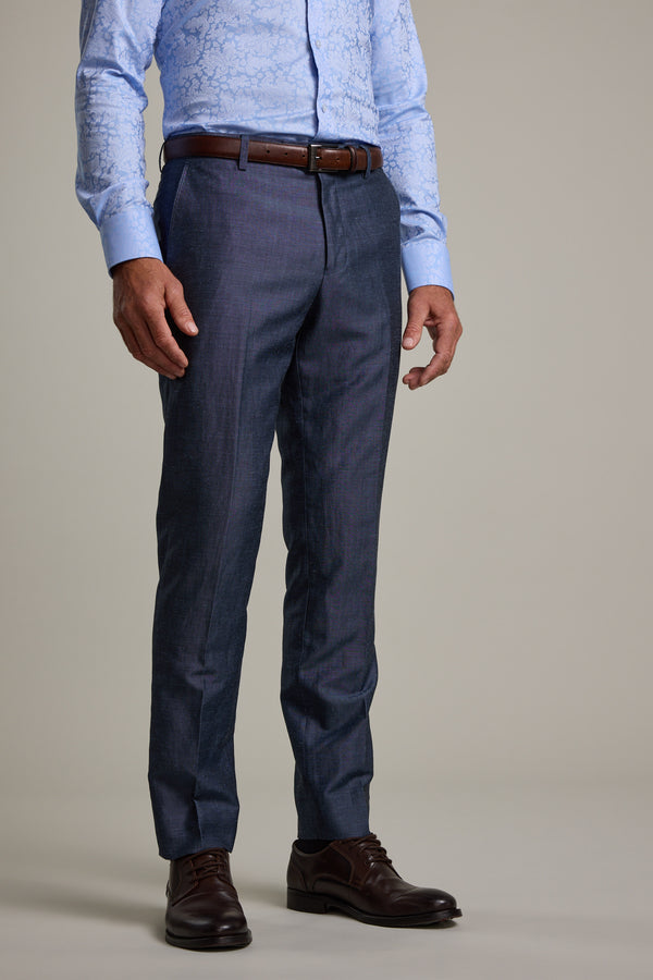 A man wears Barkers Charles Texture Suit Trouser in dark blue, a light blue patterned shirt, brown belt, and dark brown dress shoes—styled for a modern look—standing against a plain light background. Image is cropped at shoulder height.