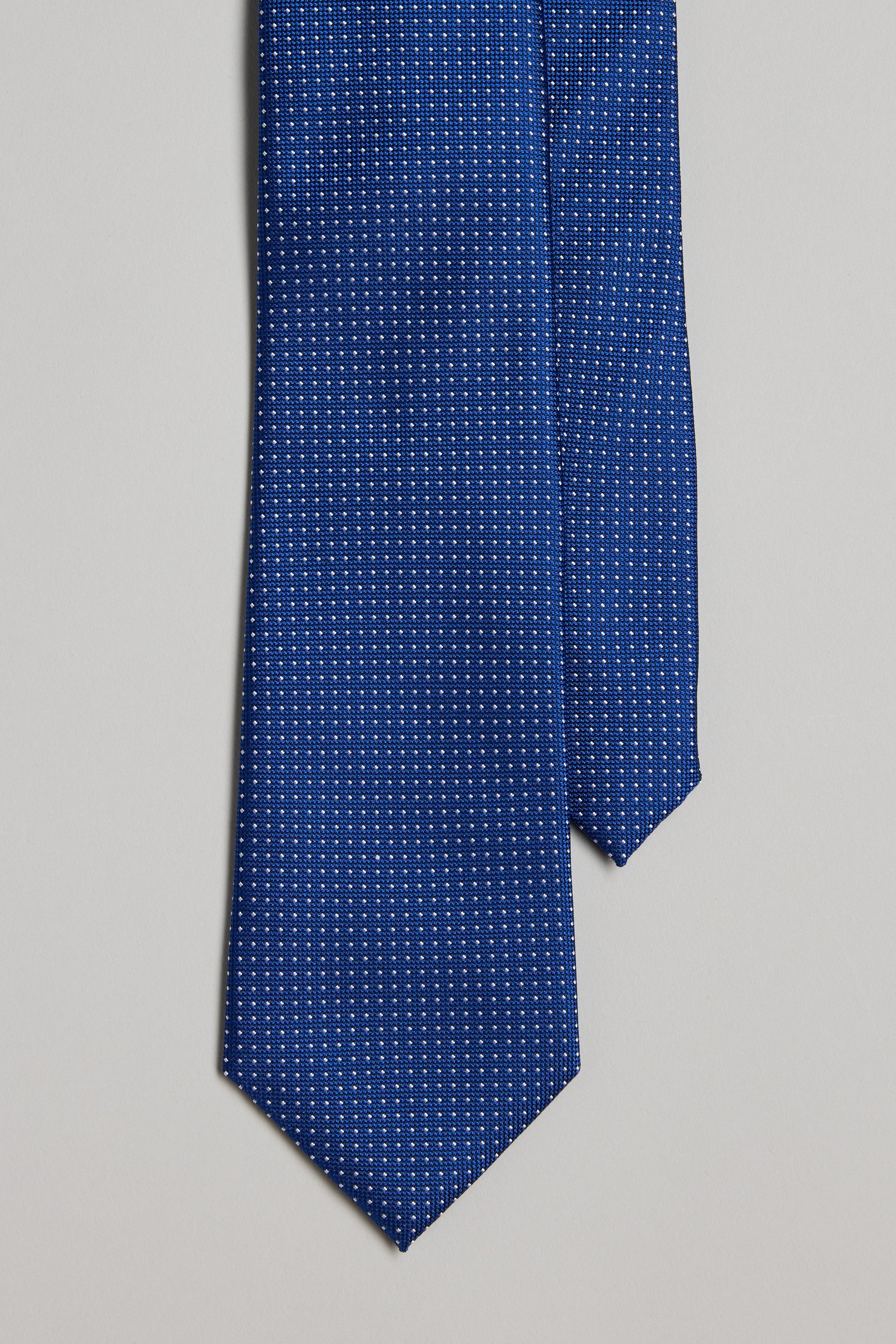The Farry Pindot Tie by Barkers features a blue silk design with small, evenly spaced white dots—an elegant accessory for those who value quality. Displayed on a light gray background.