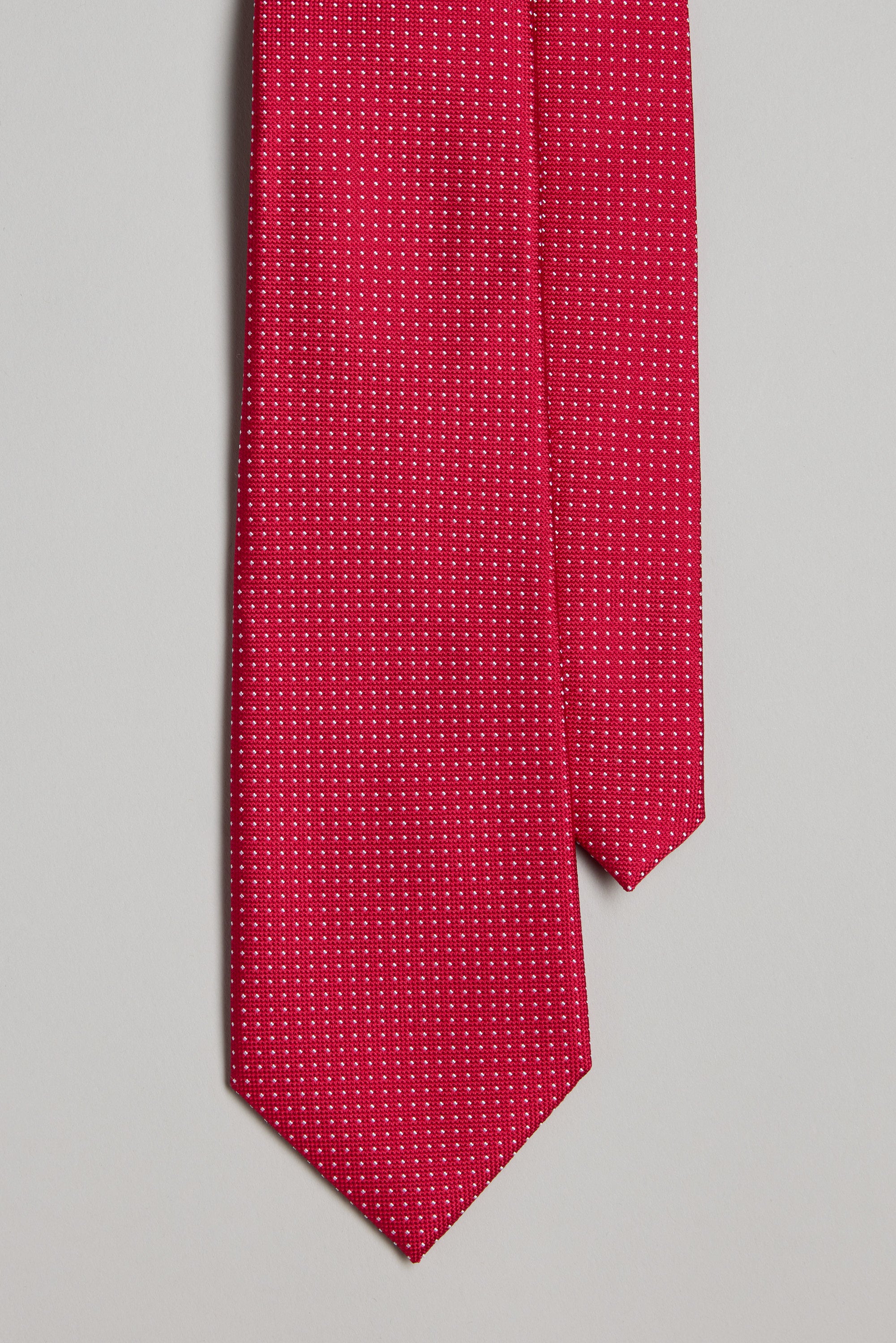 The Barkers Farry Pindot Tie, featuring a red base with tiny white dots, is displayed on a light gray background. Neatly arranged with the pointed end down, it's perfect for pairing with pocket squares or other silk accessories.