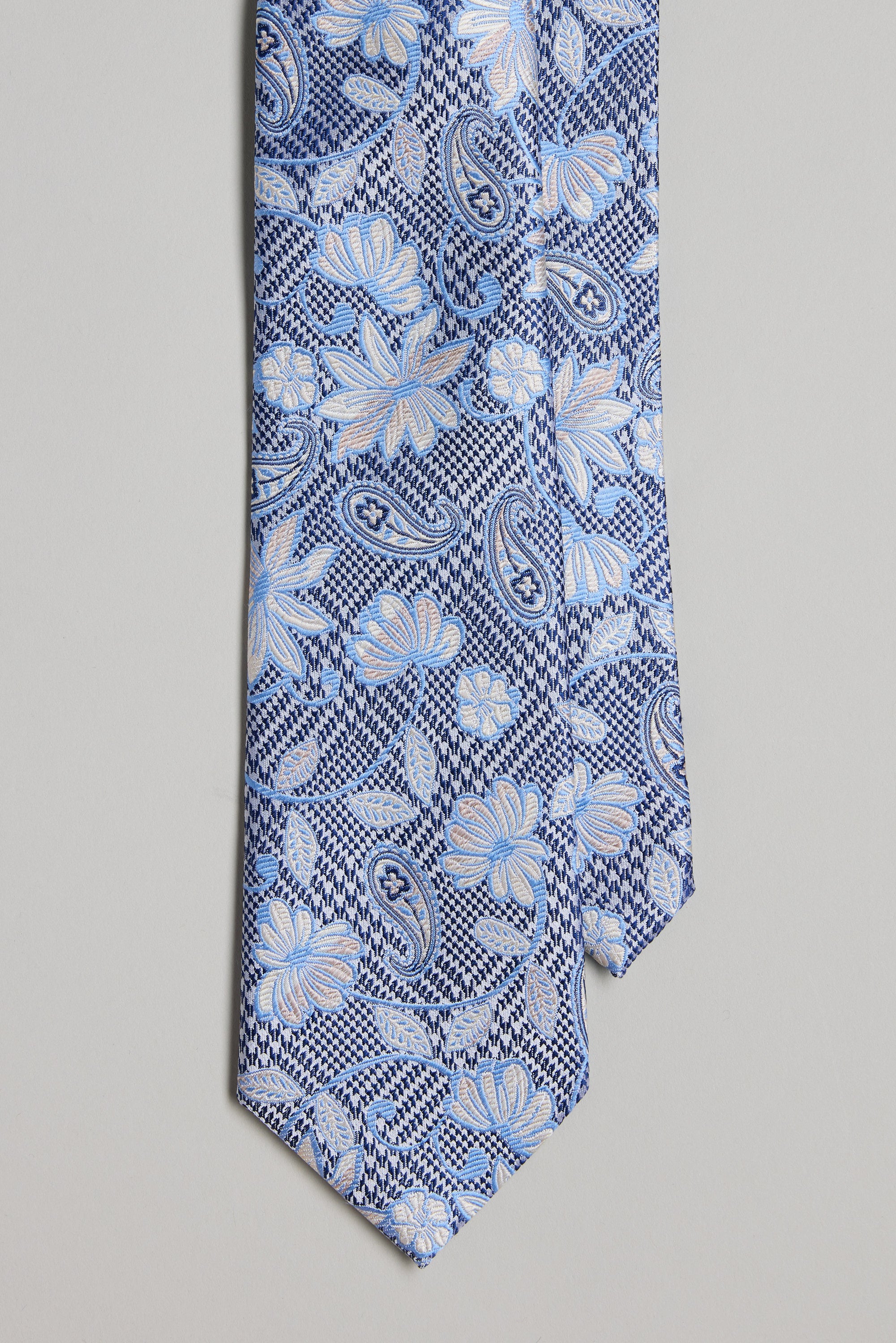 A close-up of the Barkers Platt Paisley Tie, showcasing blue silk with light blue and white floral and paisley patterns on a textured geometric background—ideal for pairing with matching pocket squares or silk accessories.