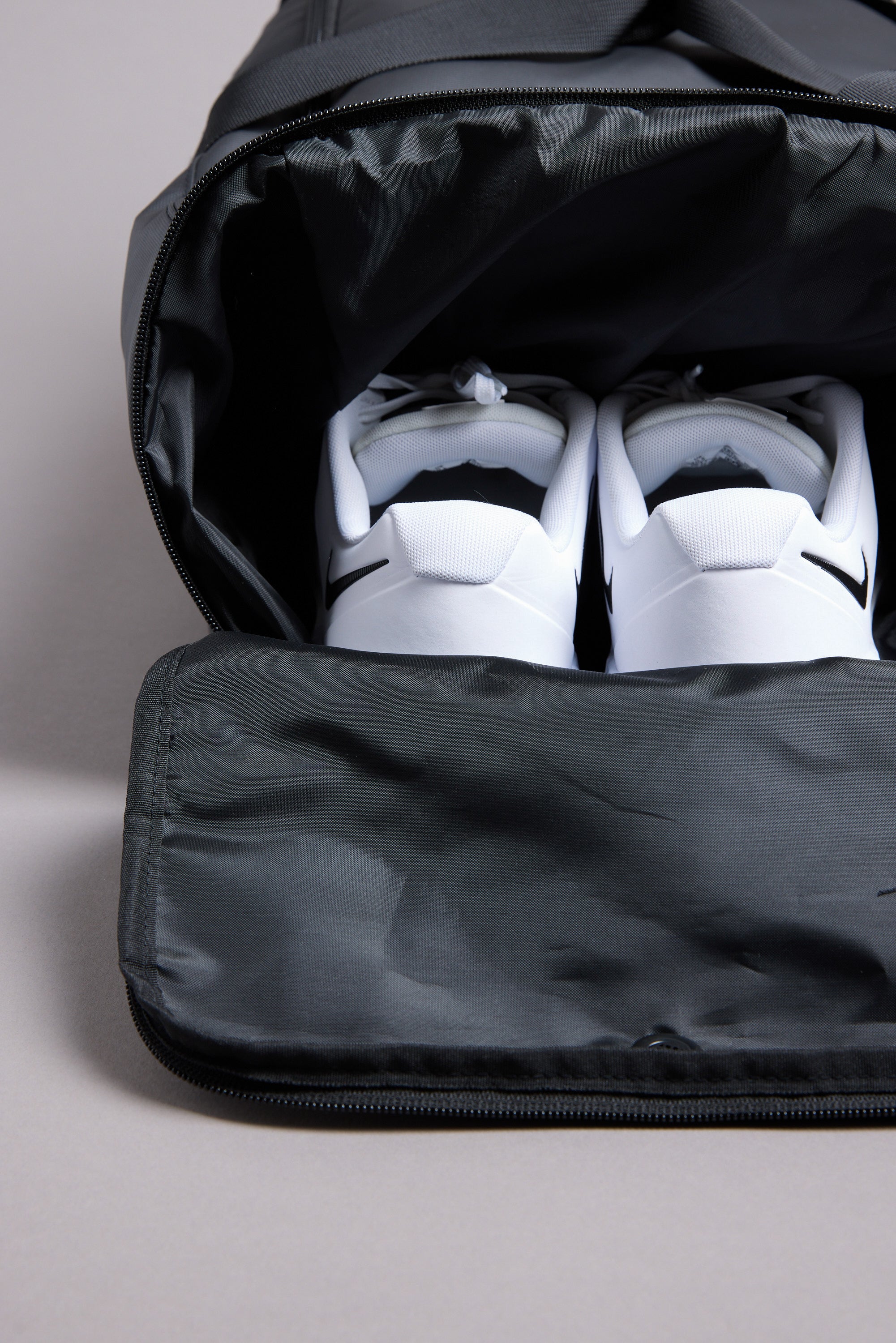 A pair of white sneakers with black accents sits inside a partially unzipped WearEver Transit Holdall by WearEver, the shoes visible from above.