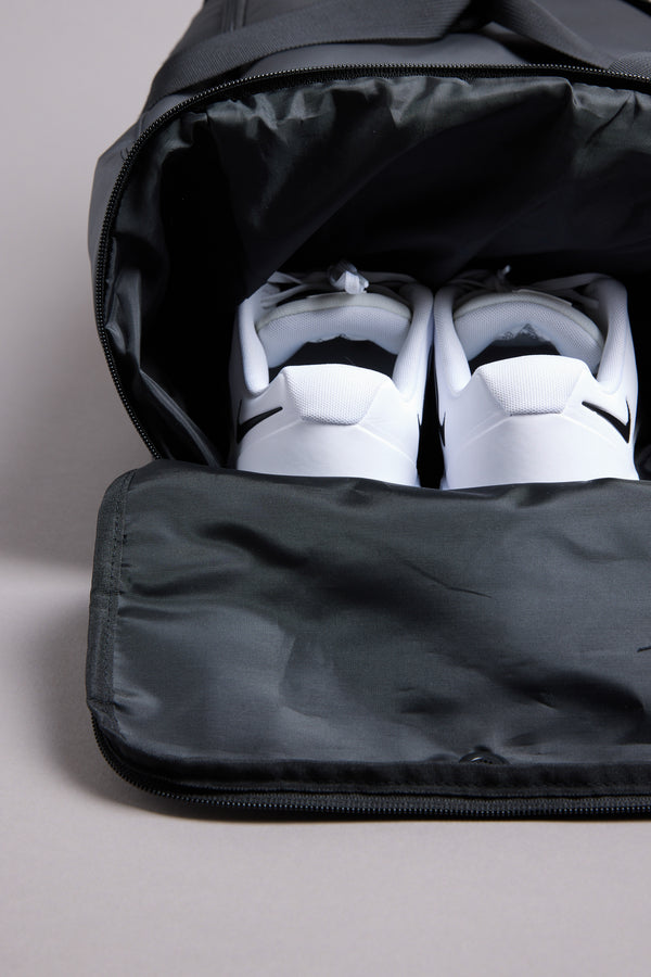 A pair of white sneakers with black accents sits inside a partially unzipped WearEver Transit Holdall by WearEver, the shoes visible from above.