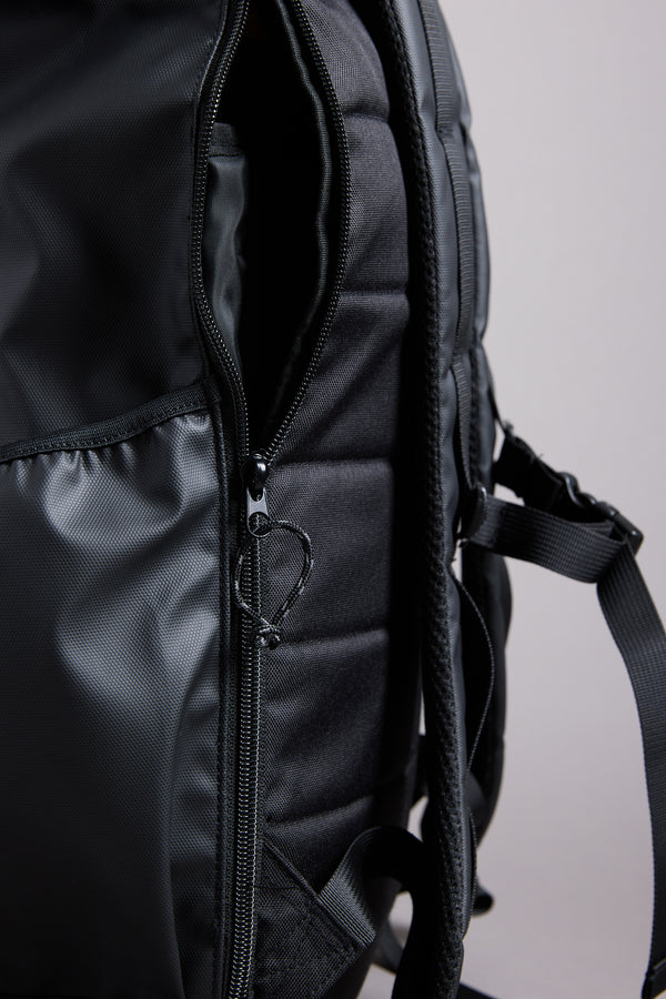 Close-up of the WearEver Transit Backpack by WearEver, featuring a partially unzipped water-resistant pocket, padded back panel, shoulder strap, and side pocket against a plain background.