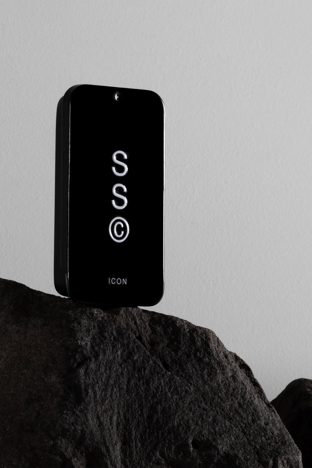 Solid State - Icon cologne sits on a dark rock with a plain light wall in the background.