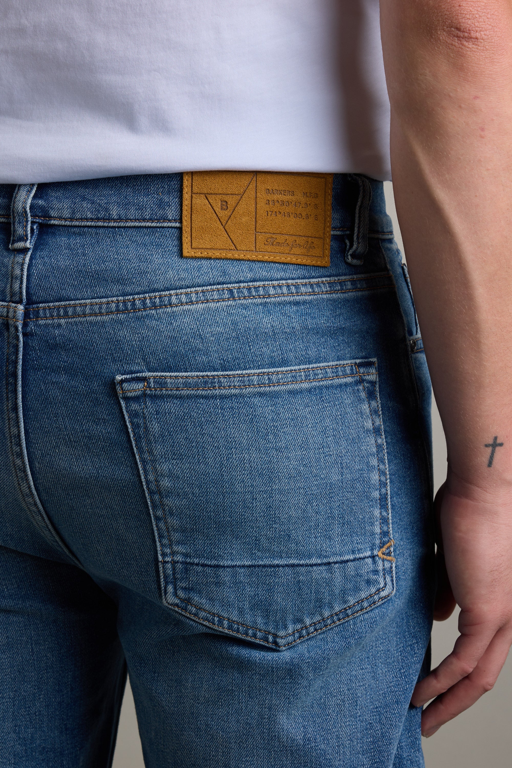 Wearing Barkers Drifter Denim Relax Jean, showing a small cross tattoo on their forearm.