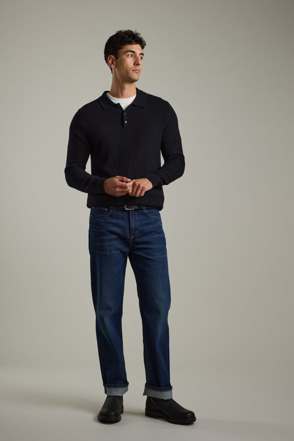 A man wears a Barkers Ainsley Woollen Long Sleeve Polo, blue jeans, and black shoes.