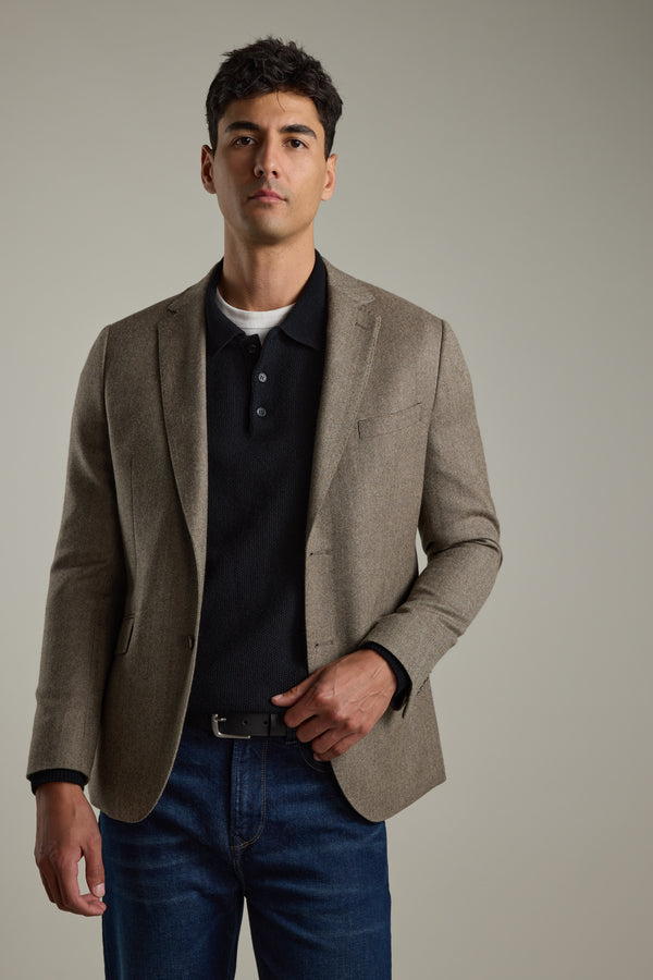 Man in a tan blazer, Barkers Ainsley Woollen Long Sleeve Polo, and jeans on light background.