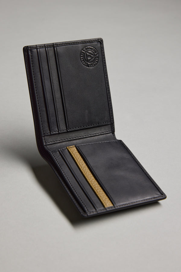 The Barkers Harris Leather Fold Wallet, crafted from black cowhide, sits open on a gray surface displaying multiple card slots, a gold-accented pocket, and an embossed circular logo inside the upper flap.