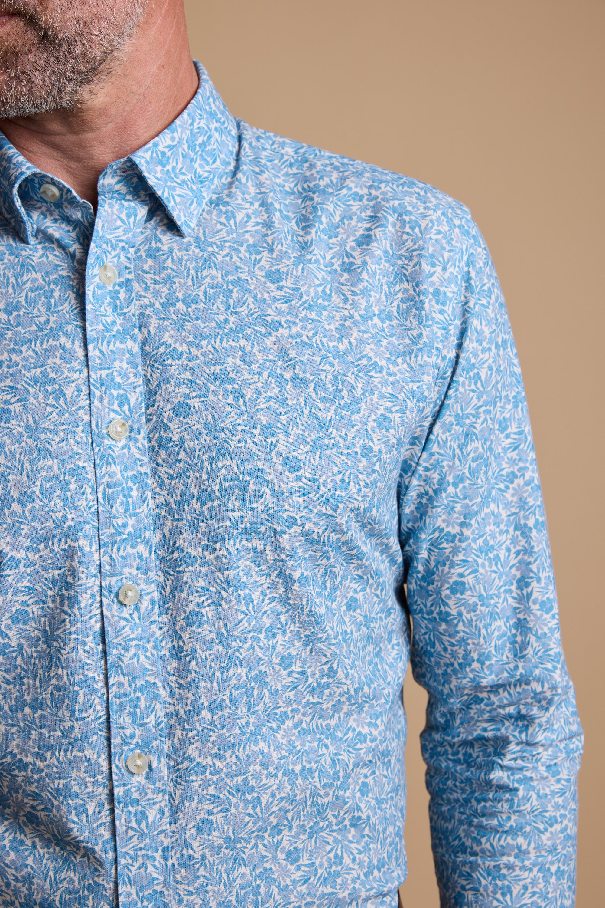 A man models the Barkers Torrey Print Shirt in light blue and white, crafted from responsibly sourced cotton. Shown from shoulders to waist against a plain beige background, his face is partially out of frame.