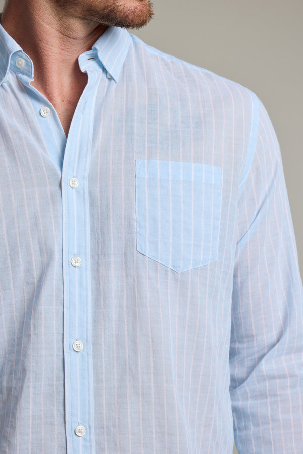 A man wears the Barkers Russell Stripe Shirt, a light blue, 100% cotton long sleeve shirt with white stripes and a chest pocket. Shown from shoulders to mid-torso, his face is partially out of frame.