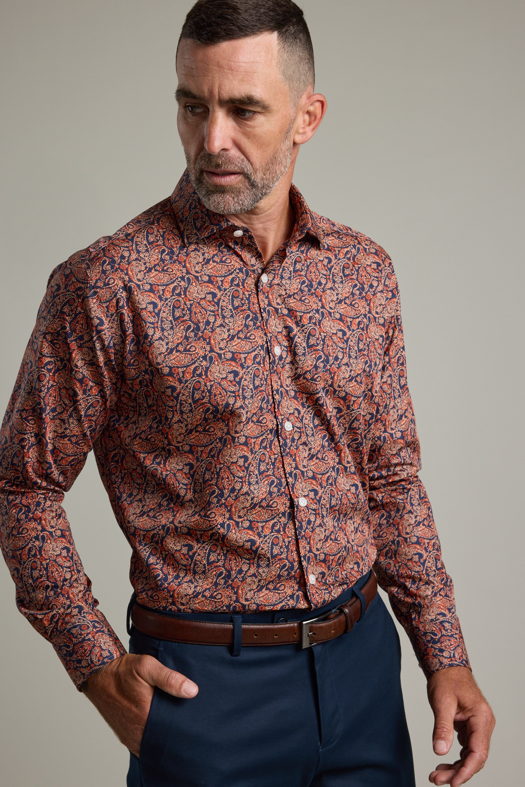 A man wearing the Barkers Paisley Business Shirt in a classic fit with a red and blue pattern, paired with navy pants and a brown belt. Crafted from Eco Easy Care fabric for effortless style.