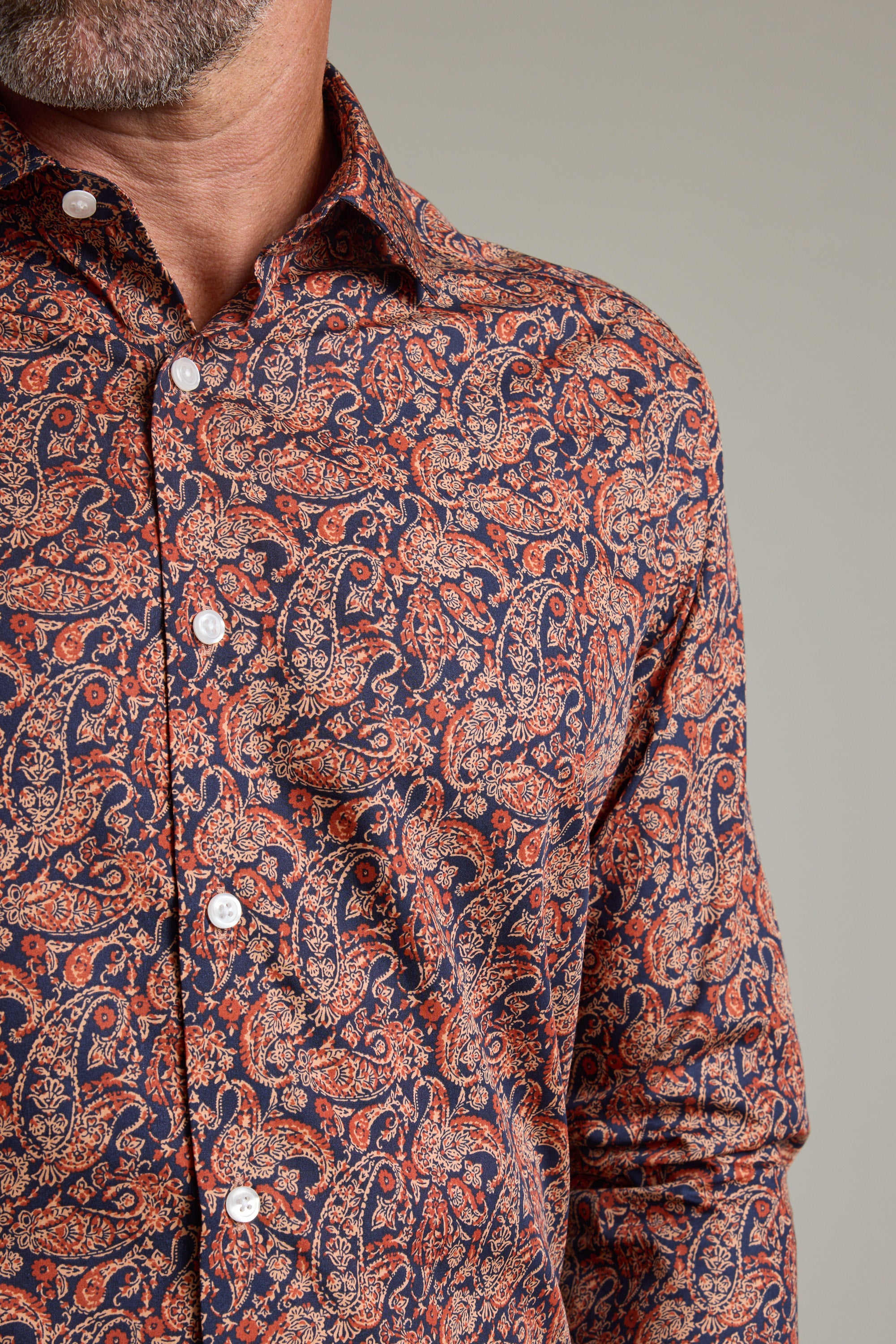 A close-up of a man’s torso wearing the Barkers Paisley Business Shirt in a classic fit, featuring vibrant red, orange, and blue patterns. Made with Eco Easy Care fabric; his face is partially visible with a short beard.