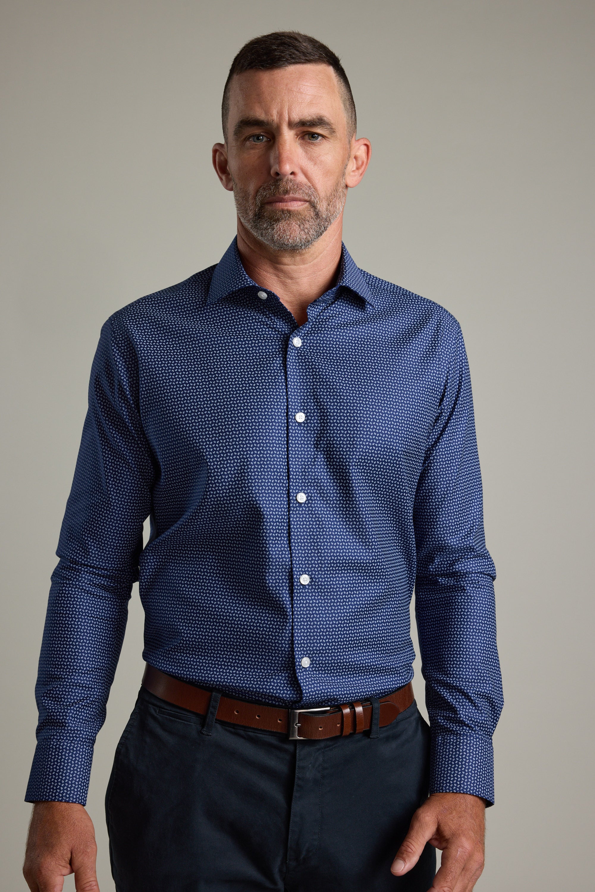 A man with short hair and a beard stands against a plain background, wearing the Barkers Maiden Paisley Business Shirt in a tailored fit, paired with dark pants and a brown belt, looking directly at the camera with a neutral expression.