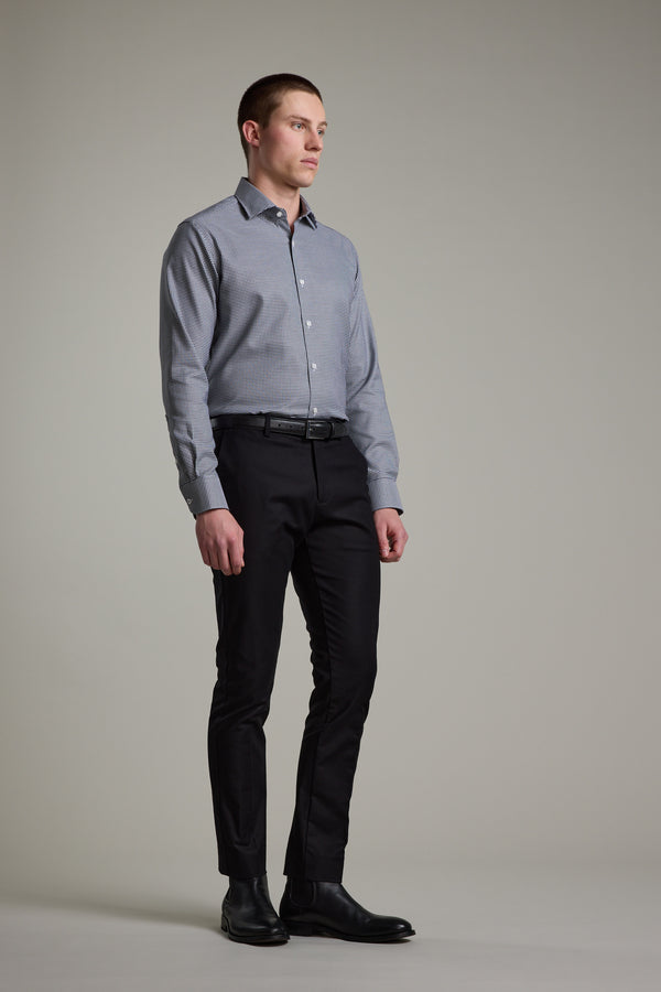 A man stands against a plain background wearing the Barkers Mitchel Check Business Shirt in a tailored fit, paired with black pants and dress shoes. He faces slightly sideways, arms relaxed and expression neutral.