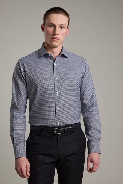 A young man with short hair stands against a plain background, wearing the Barkers Mitchel Check Business Shirt tucked into tailored black pants with a sleek belt.