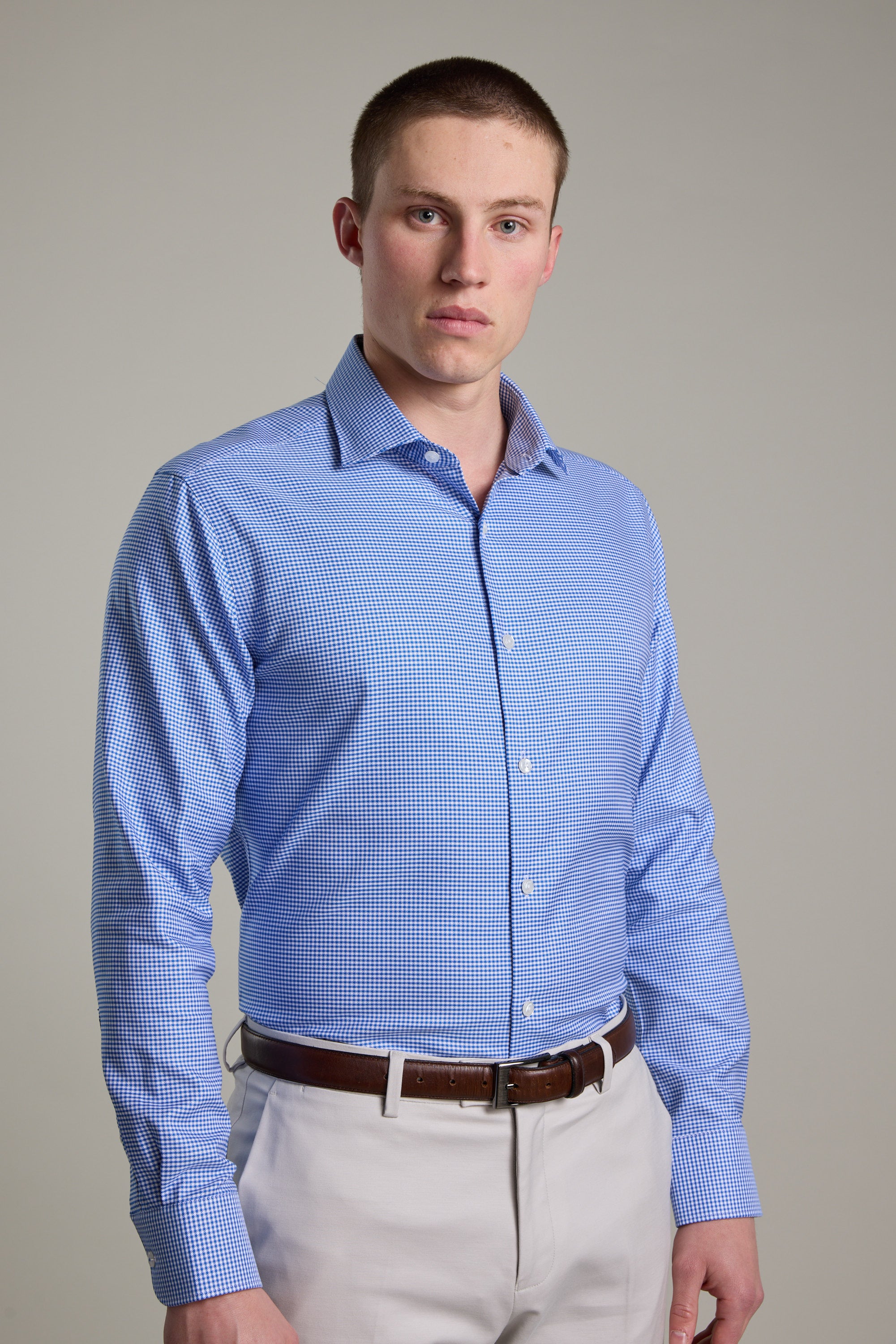 A man with short brown hair wears the Barkers Mitchel Check Business Shirt in light blue and beige pants, standing against a plain light gray background and looking directly at the camera with a neutral expression.