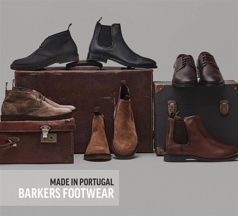 A display of mens boots and dress shoes in black, brown, and tan, arranged on vintage suitcases against a gray background. Text at the bottom reads: Made in Portugal Barkers Footwear.