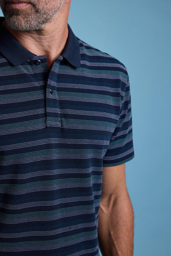 A close-up shows a man wearing the Barkers Dalton Stripe Polo in navy with teal and white stripes, made from organic cotton. Only his lower face and upper torso are visible against a light blue background—ideal for summer style.