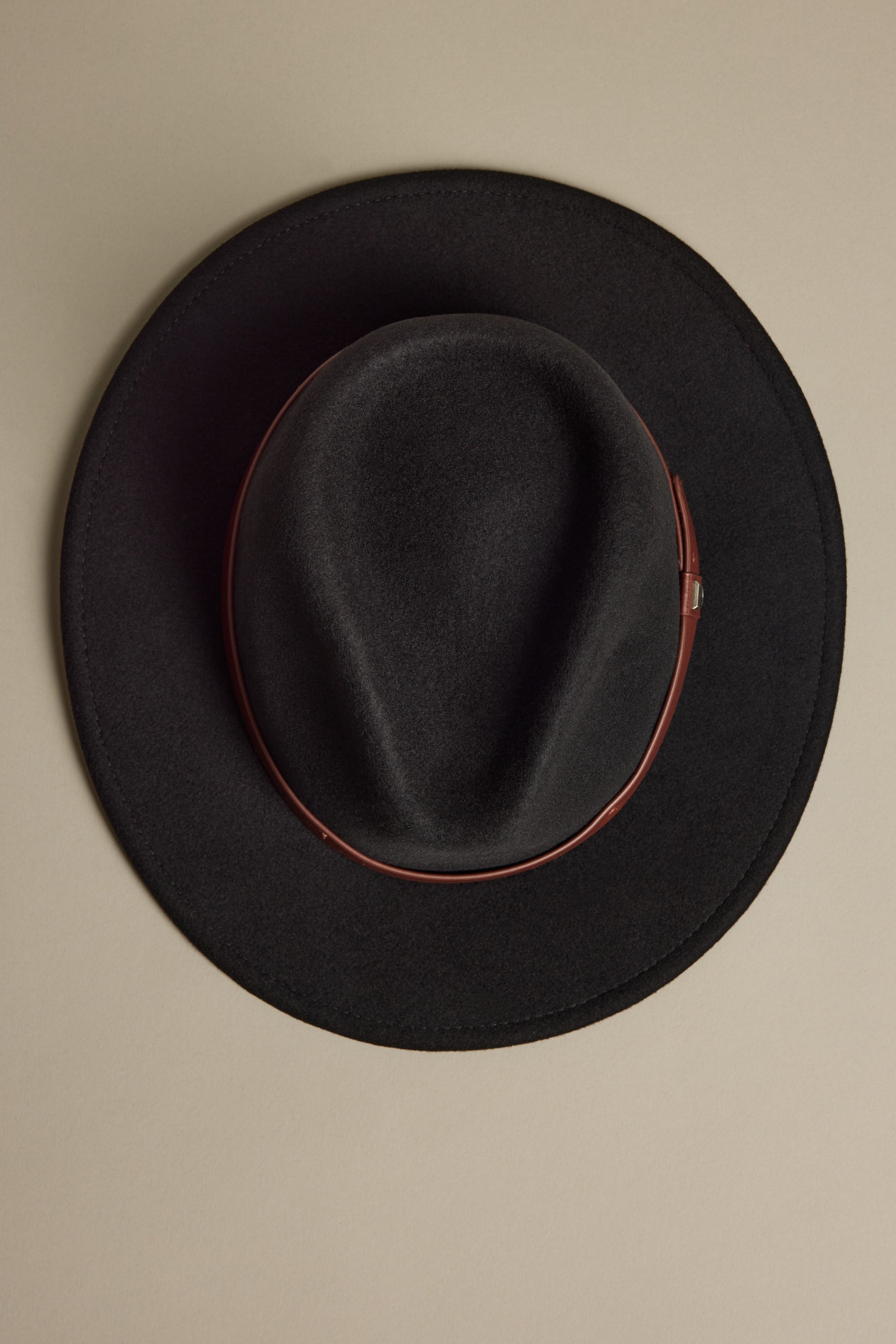 The Brixton Messer Fedora Hat by Brixton, featuring black wool felt and a brown leather band, is photographed from above on a beige background.
