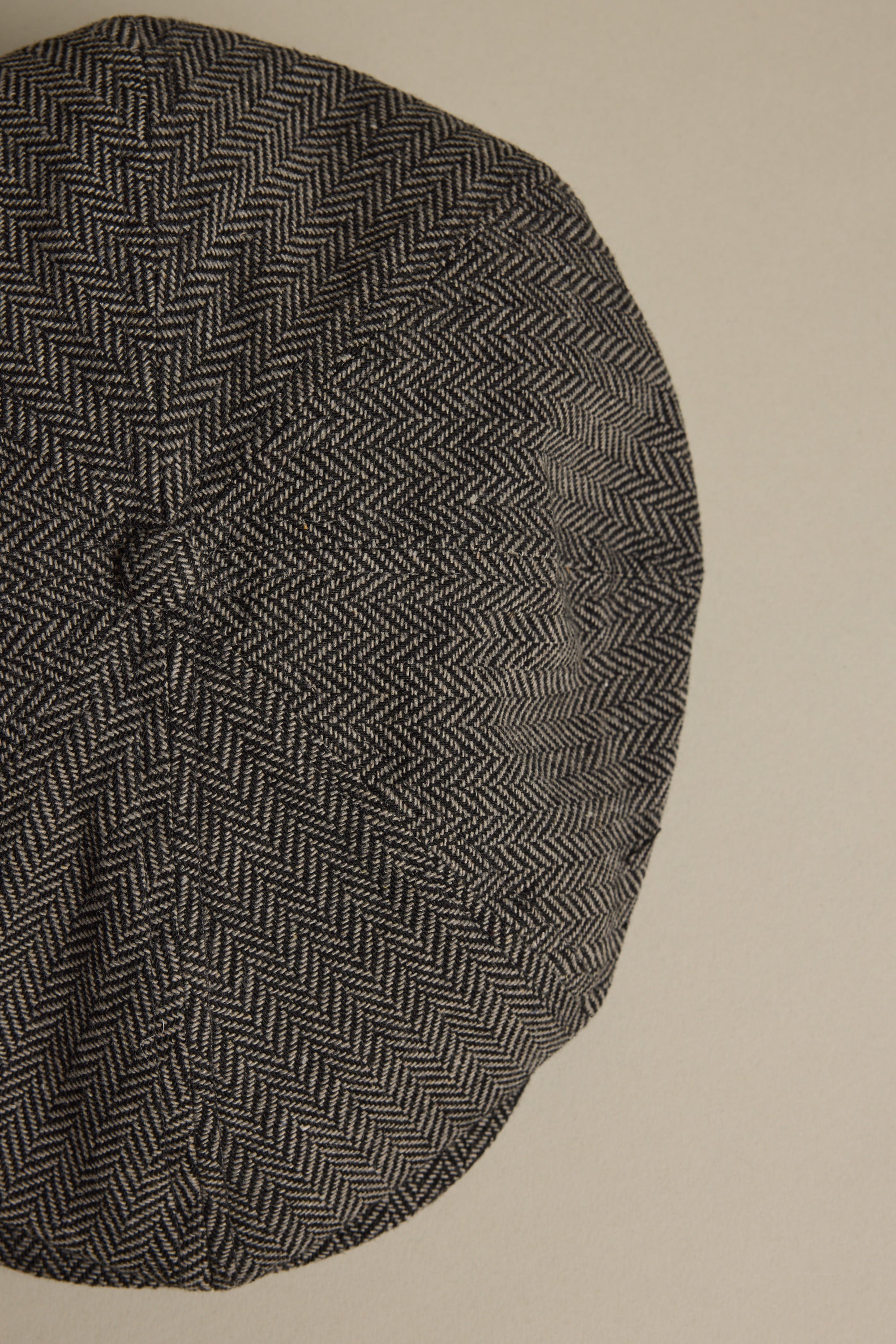 A close-up of the Brixton Brood Snap Cap by Brixton, featuring a black and white herringbone wool blend, displayed against a plain beige background.