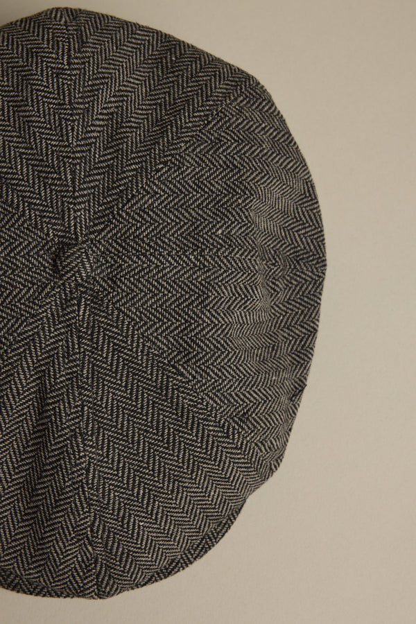 A close-up of the Brixton Brood Snap Cap by Brixton, featuring a black and white herringbone wool blend, displayed against a plain beige background.