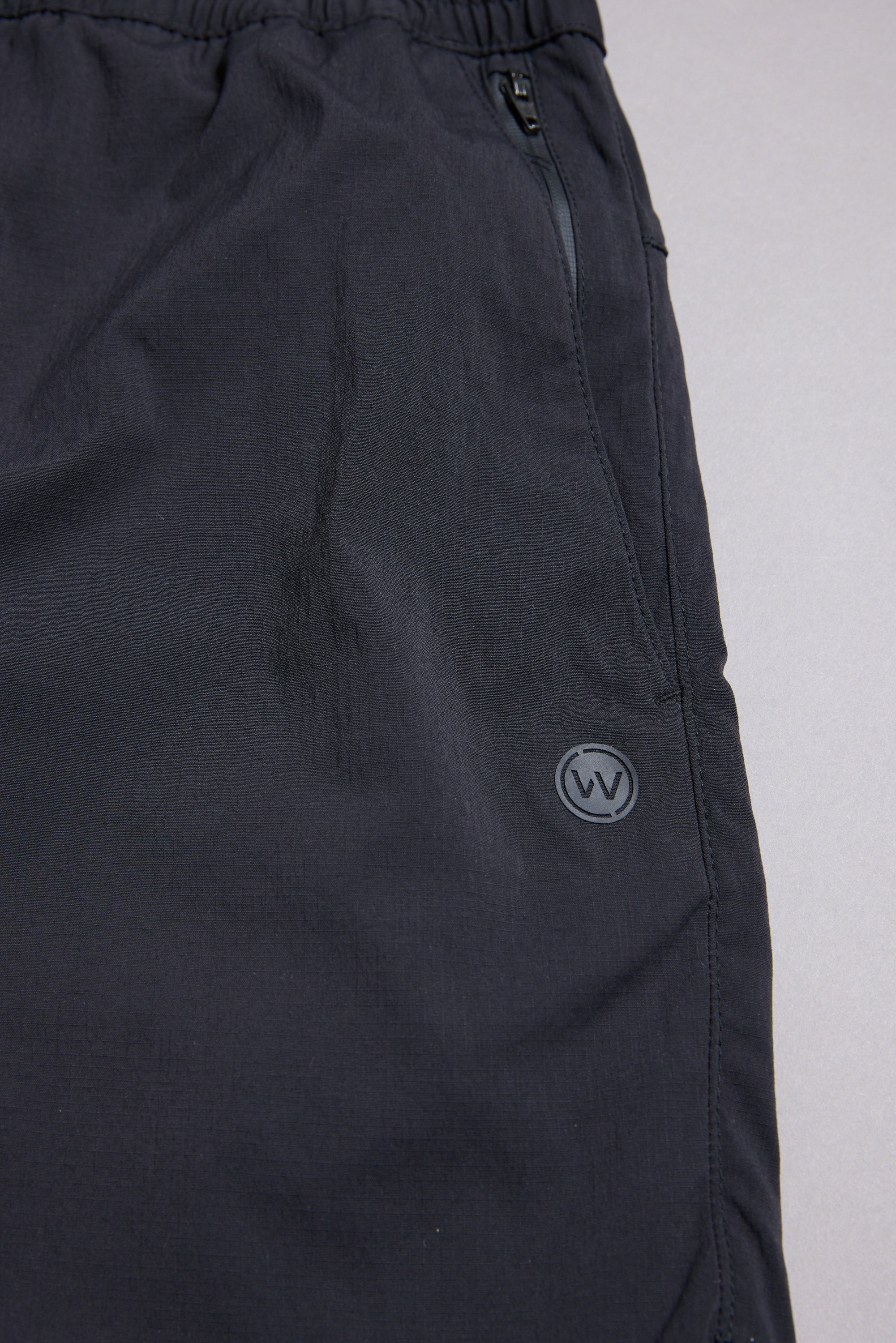 Close-up of the WearEver Agile Short by WearEver, featuring an elastic waistband, zippered side pocket, and small circular W logo on the upper thigh. Made from smooth matte fabric, these lightweight shorts offer all-day comfort with a 7-inch inseam.