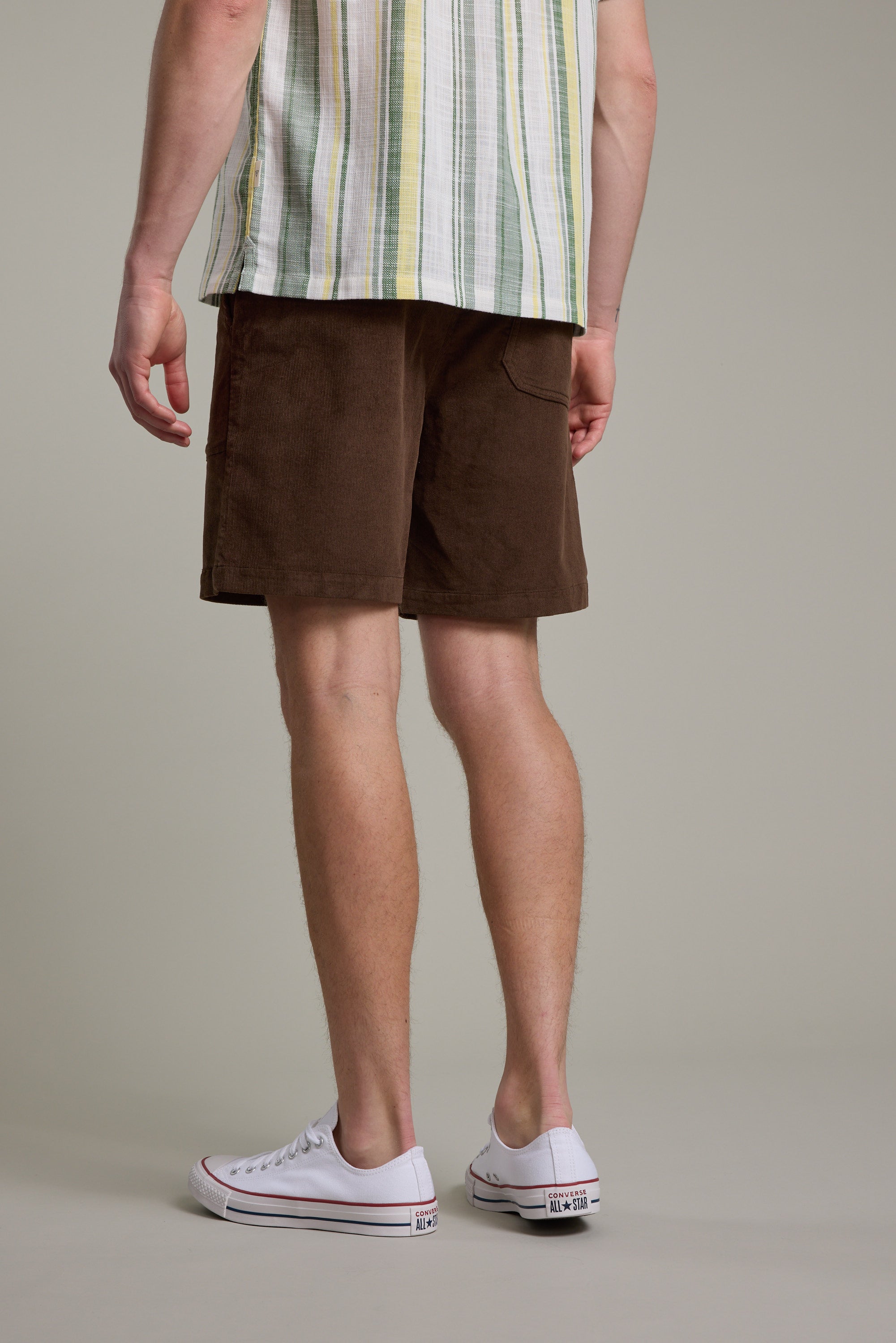 Only the lower body is visible, showcasing Barkers Montauk Cord Weekend Short with an elastic waistband, paired with a short-sleeved striped shirt and white low-top sneakers against a plain background.