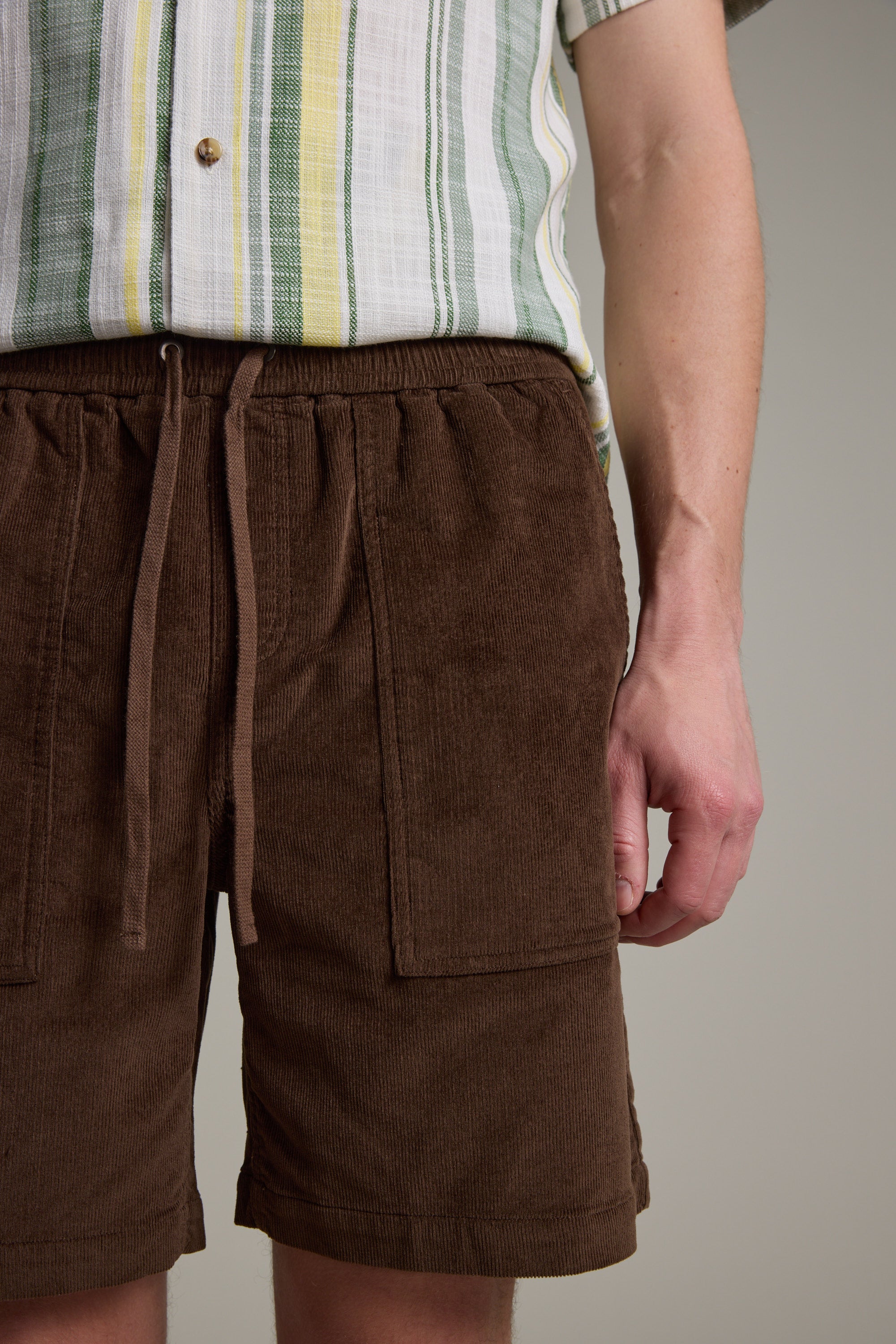 A person wearing a striped short-sleeve shirt and Barkers Montauk Cord Weekend Shorts with an elastic waistband stands against a plain background, showing only the torso and upper legs.