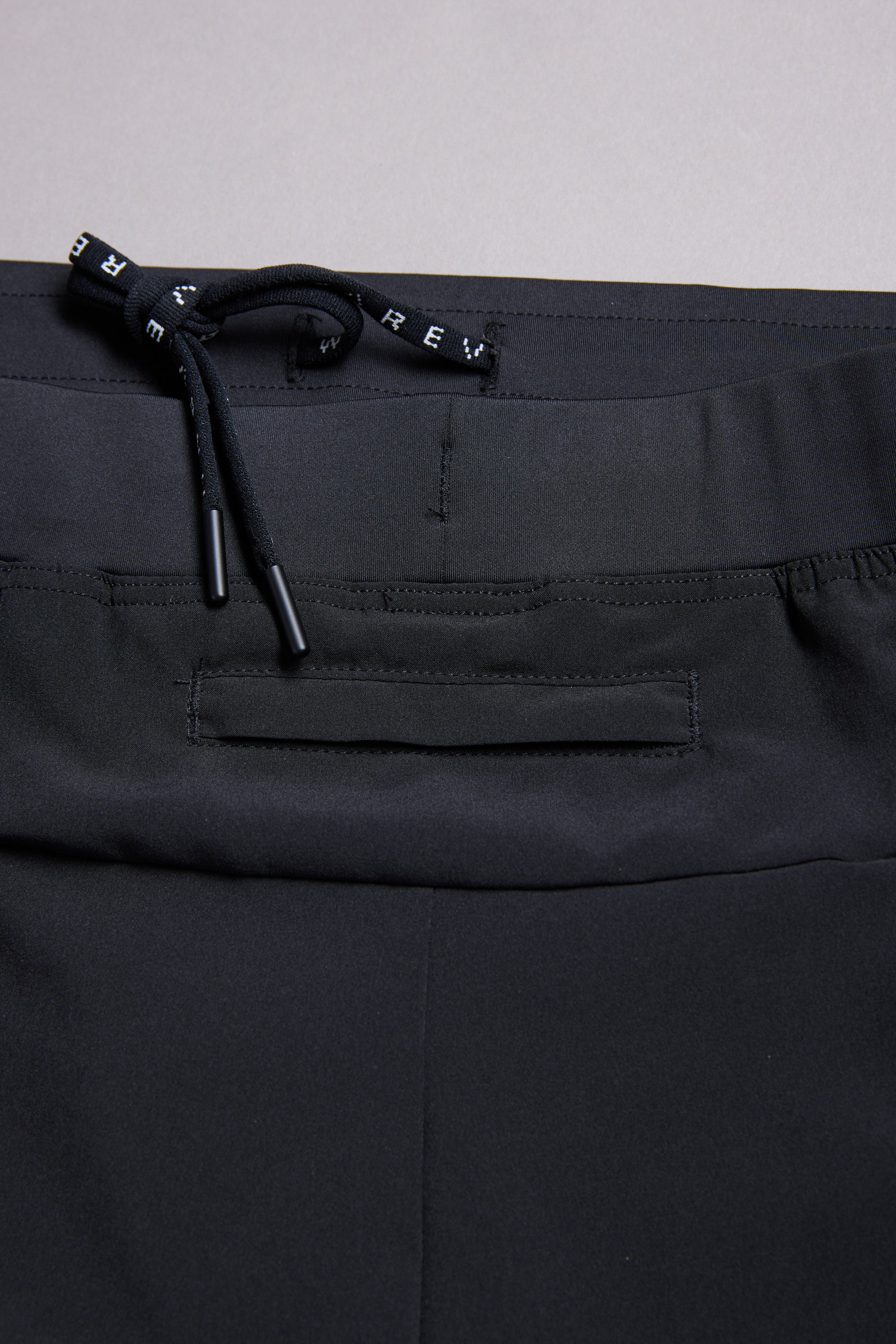 Close-up of the waistband and upper section of WearEver Cadence Short in black, featuring a drawstring and horizontal back pocket, set against a neutral background.