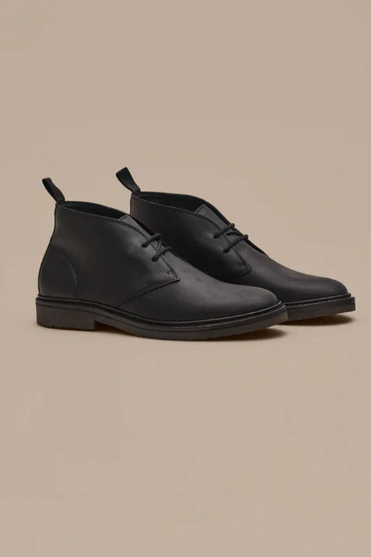 The Barkers Howarth Desert Boot is a pair of black leather boots with pull tabs, featuring a sleek, minimalist design inspired by classic desert boots—an excellent showcase of quality Portuguese footwear.