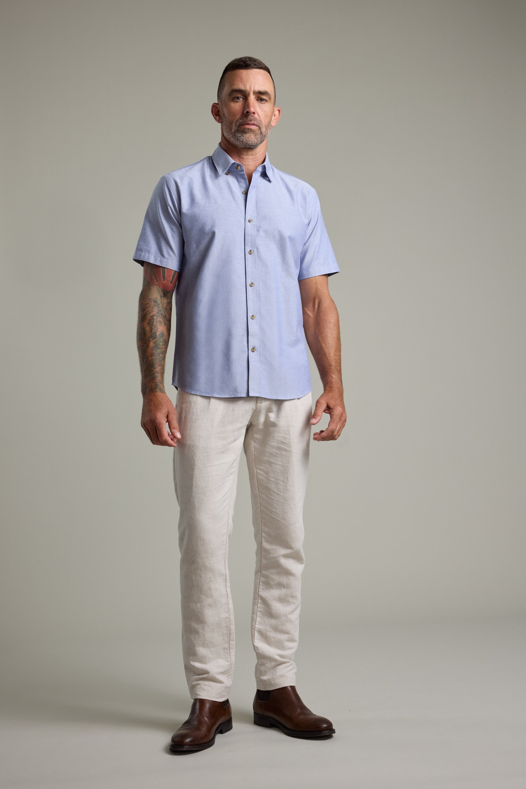 Man in Barkers Archer Oxford Shirt, beige pants, and brown boots stands.