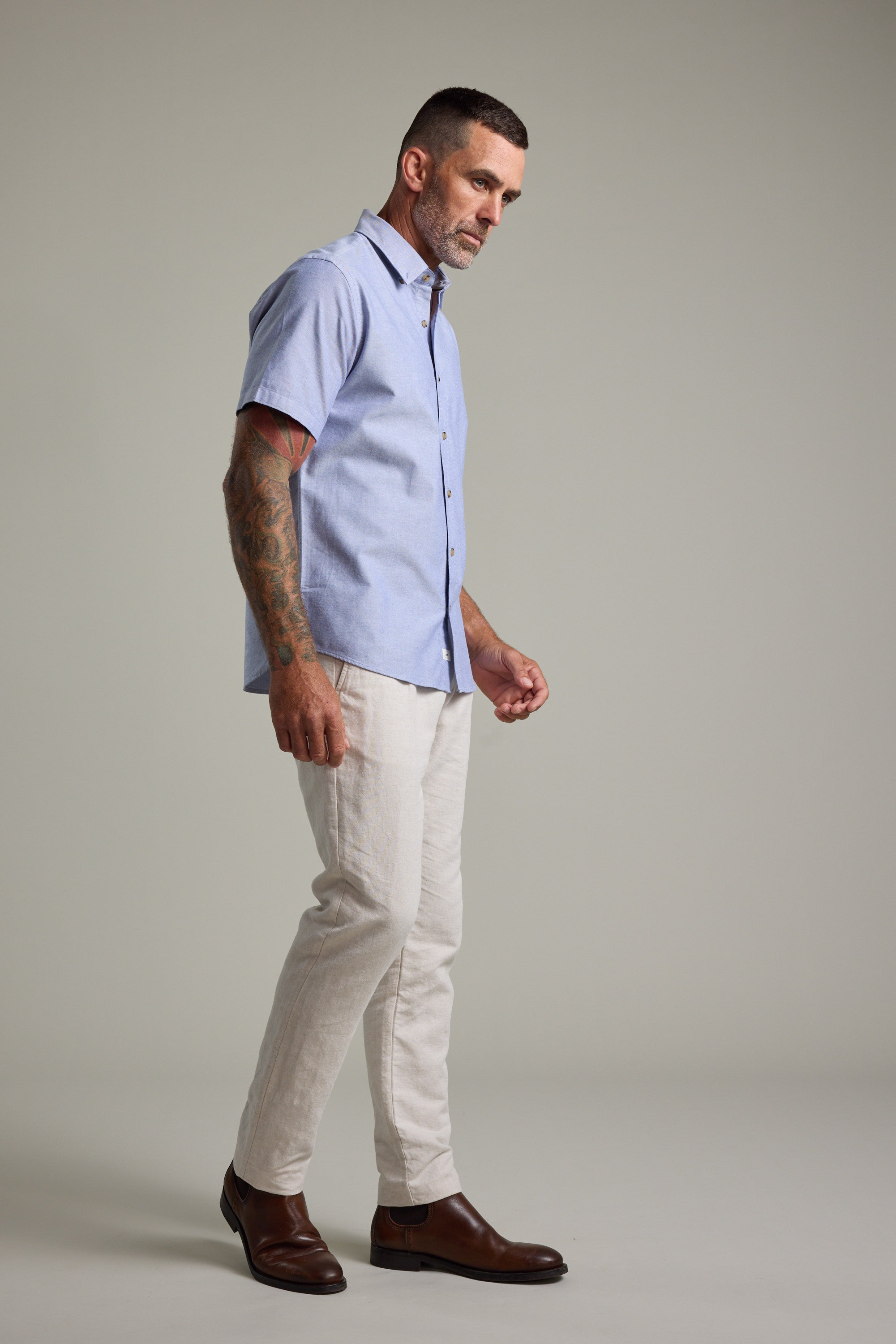 Man wearing Barkers Archer Oxford Shirt, beige pants, and brown shoes, standing sideways.