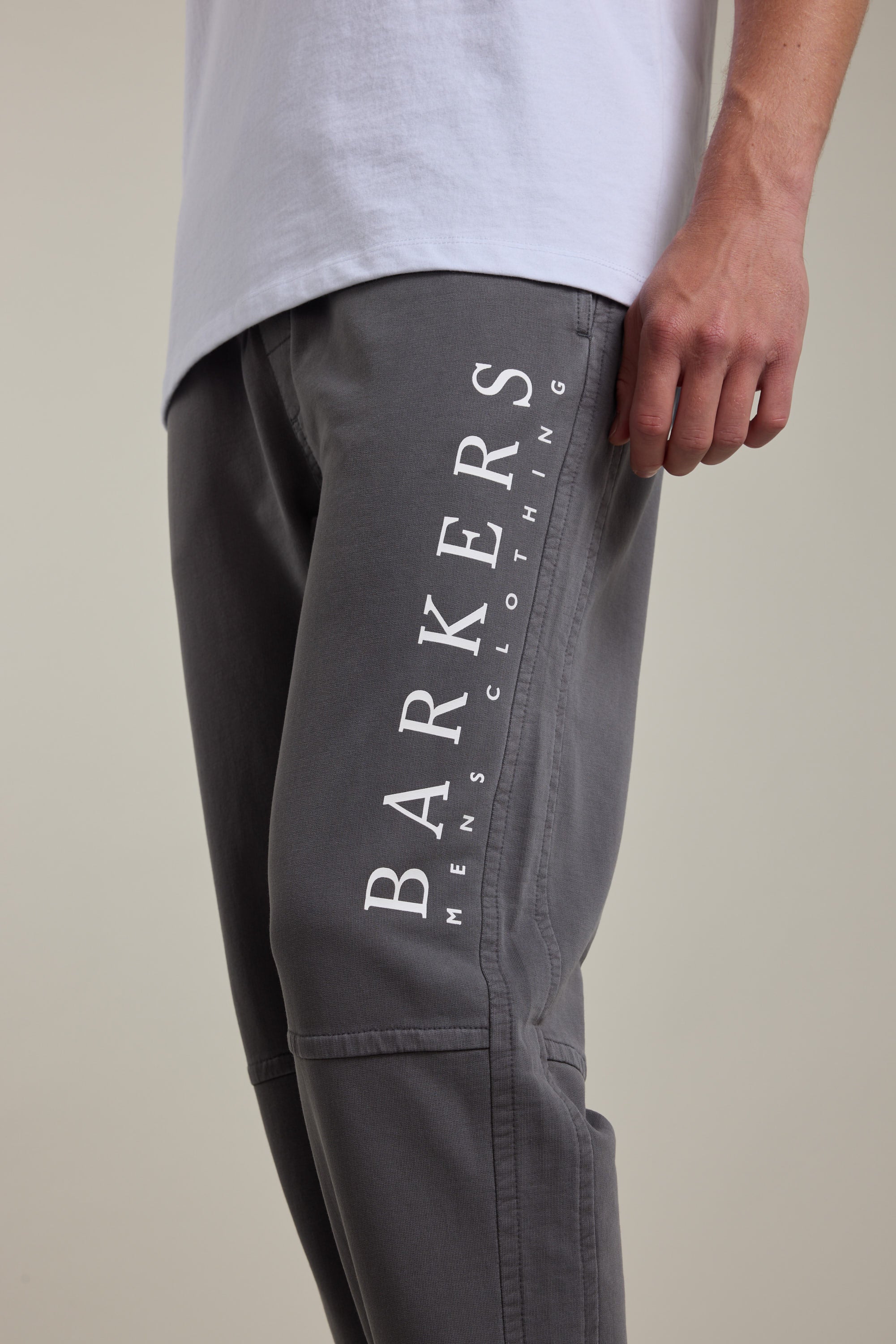 A person wearing Barkers’ Organic Classic Print Track Pant in grey, with "BARKERS MENS CLOTHING" printed vertically on the thigh and paired with a white shirt. Only the torso and upper legs are shown.