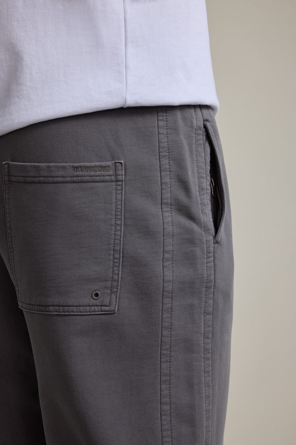 Close-up of a person wearing Barkers Organic Classic Print Track Pant in gray, featuring a side pocket, visible stitching, and the Barkers logo stitched above the back pocket. Paired with a white shirt against a neutral background.