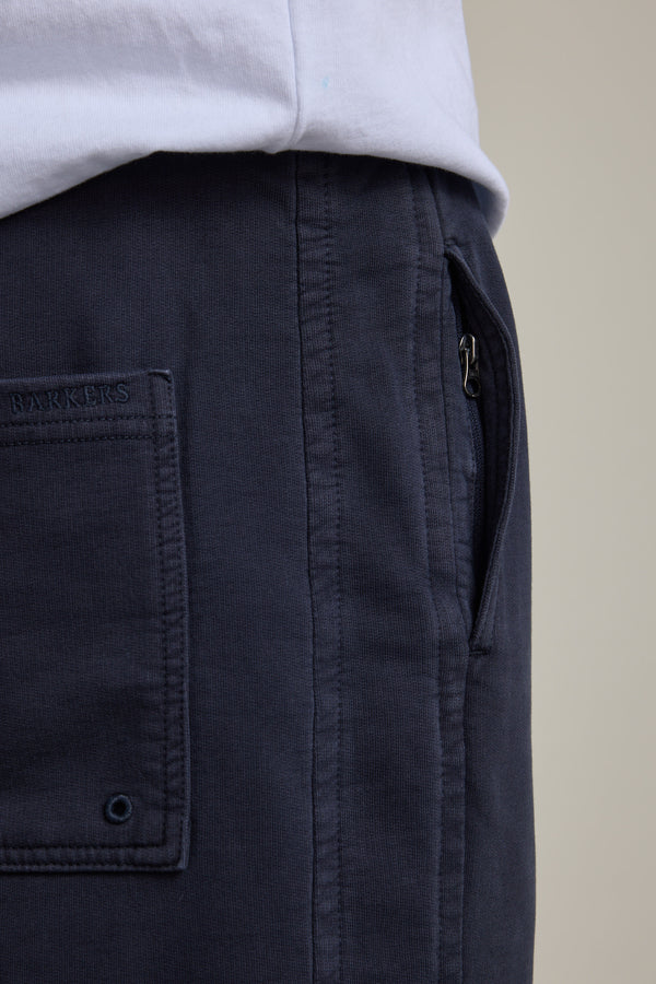 Close-up of a person wearing Barkers Organic Classic Print Track Pant in navy blue, featuring a side zipper pocket and visible back pocket, paired with a white shirt neatly tucked at the waist.